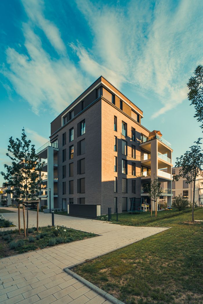 why-choose-us Contemporary apartment building exterior with landscaped surroundings under a clear sky.